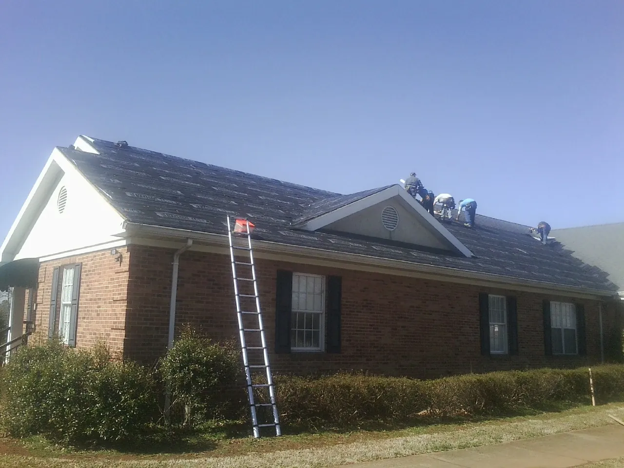 Crew tearing shingles off a brick ranch roof with a ladder set — Metal Roof Repair work by our crew in Cullen