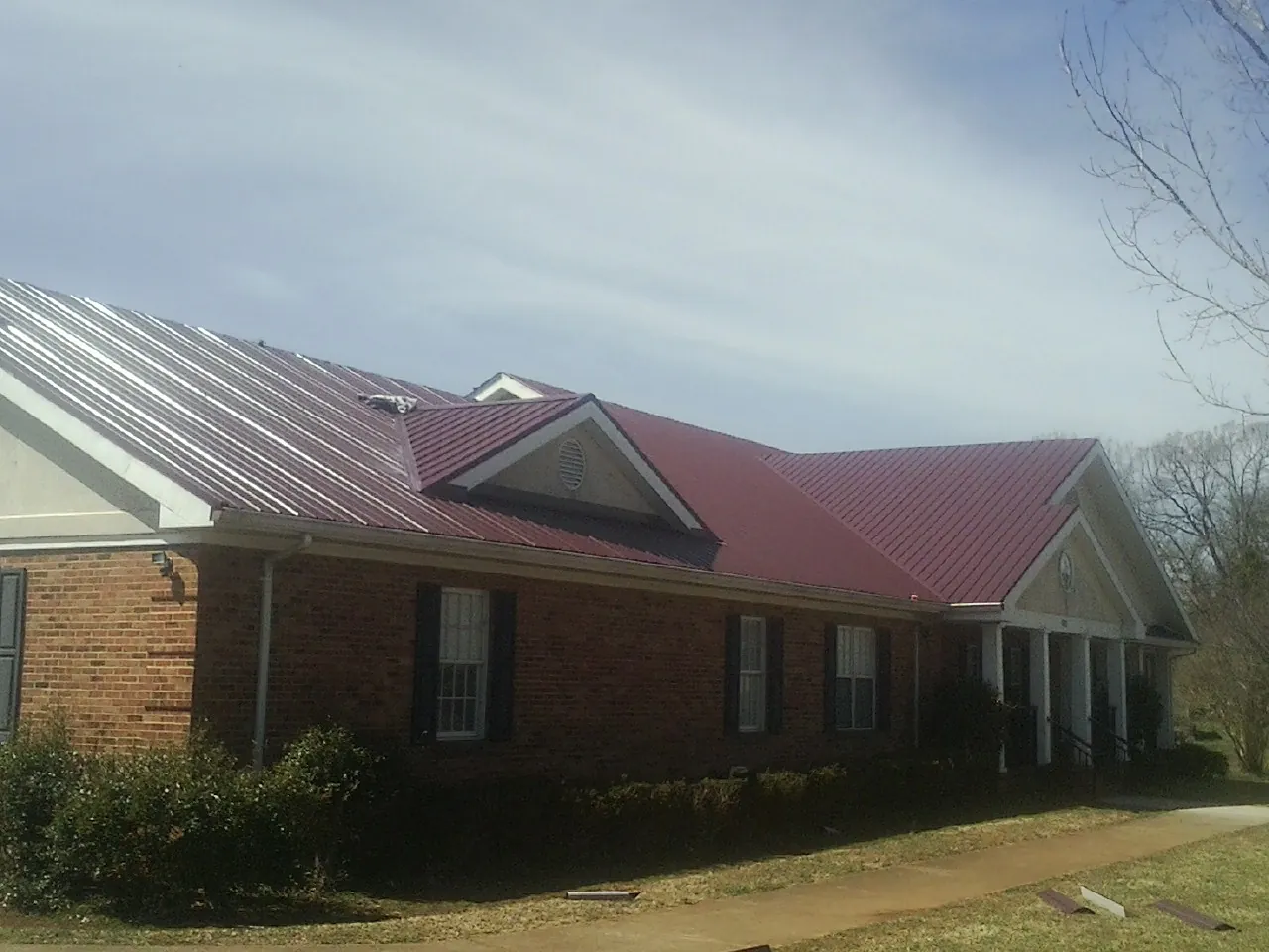 Red metal roof with gabled entries on a long brick building, from a Hail Damage Roof Repair job in Cullen