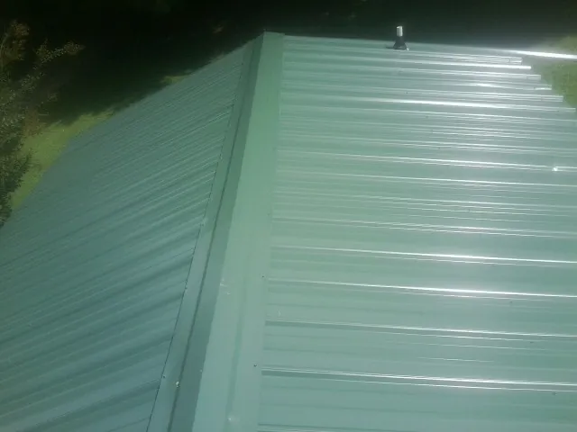 New green metal panels meeting at the ridge of a roof — Flat Roof Repair work by our crew in Cullen