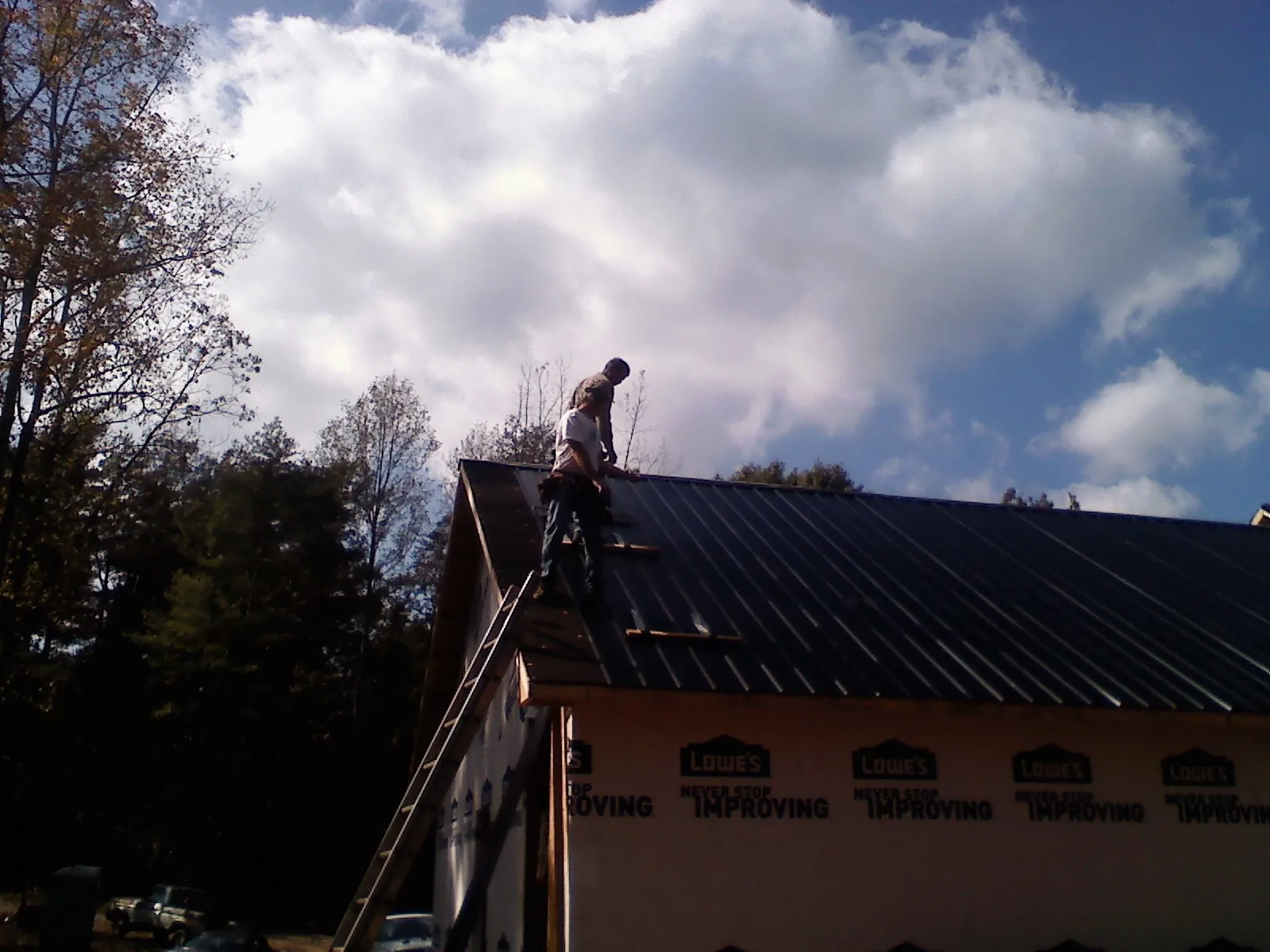 Roofer fastening dark metal panels high against a cloudy sky, from a Roof Inspection job in Cullen