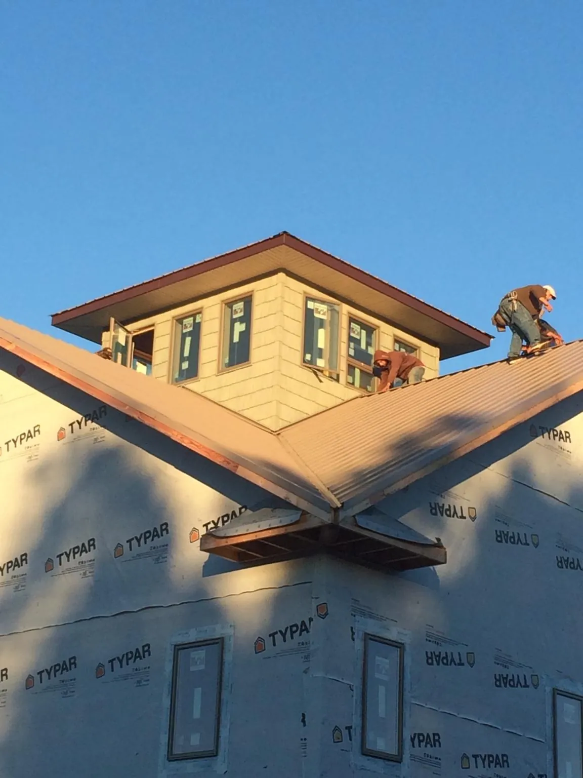 Roofers working around a rooftop cupola on a new metal roof at sunset — Roof Waterproofing in Cullen by Roofing Brothers